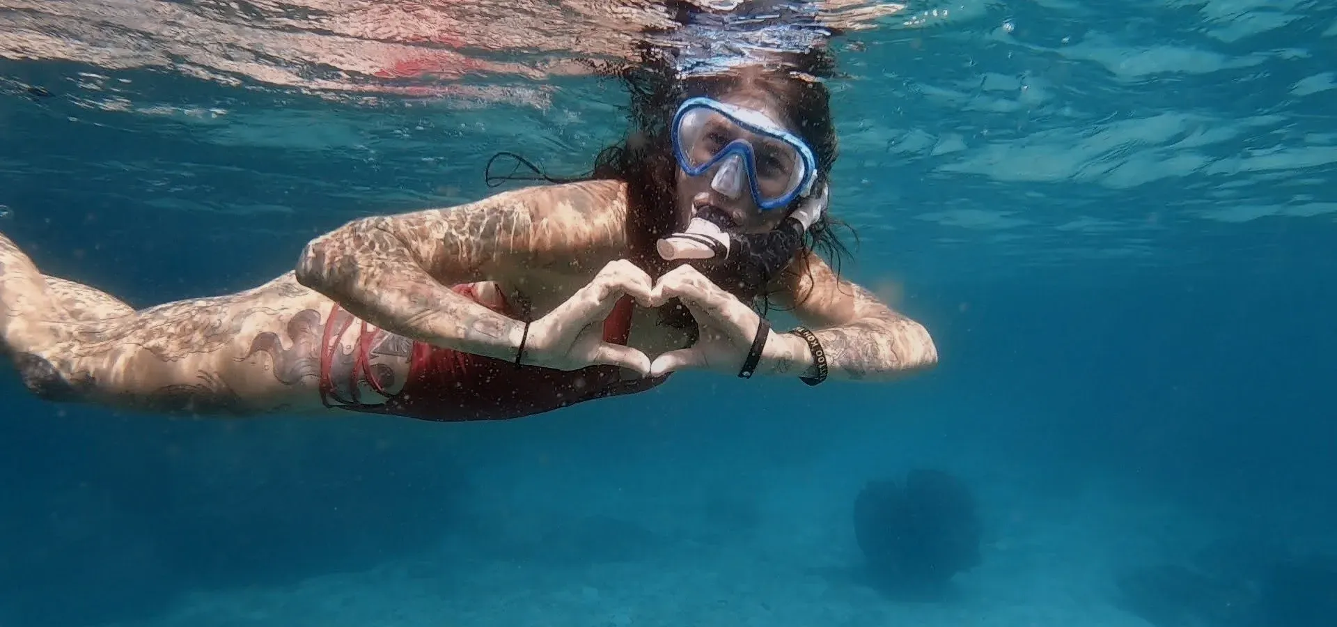 Schnorchlerin formt mit den Händen ein Herz im türkisfarbenen Wasser vor Koh Tao